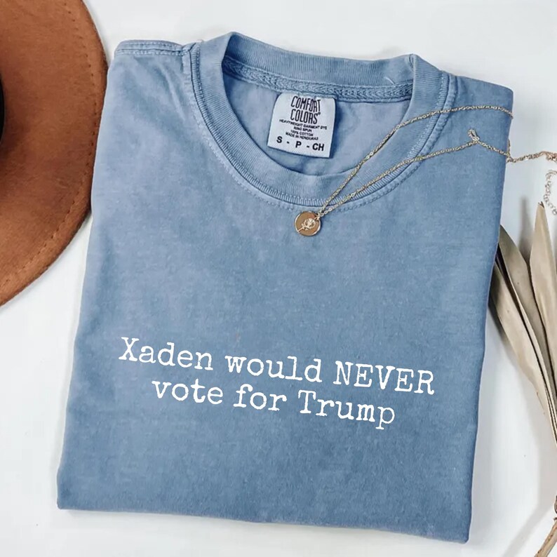 May include: A light blue t-shirt with the text "Xaden would NEVER vote for Trump" printed in white.