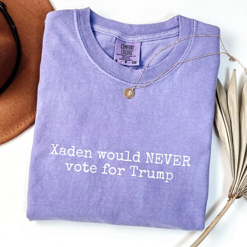 May include: A purple t-shirt with the text "Xaden would NEVER vote for Trump" printed in white.