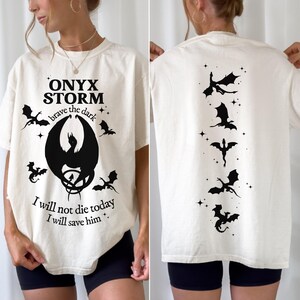 May include: A white t-shirt with a black dragon graphic on the front and a row of black dragons on the back. The front graphic includes the text "ONYX STORM" and "brave the dark". The text "I will not die today. I will save him." is also printed on the front.
