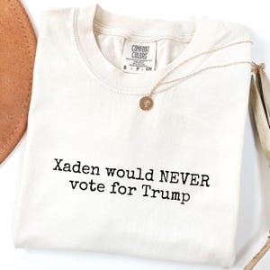 May include: A white t-shirt with the text "Xaden would NEVER vote for Trump" printed in black.