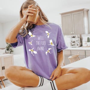 May include: Purple t-shirt with a white graphic of dragons and the text "Well the fuck aware".