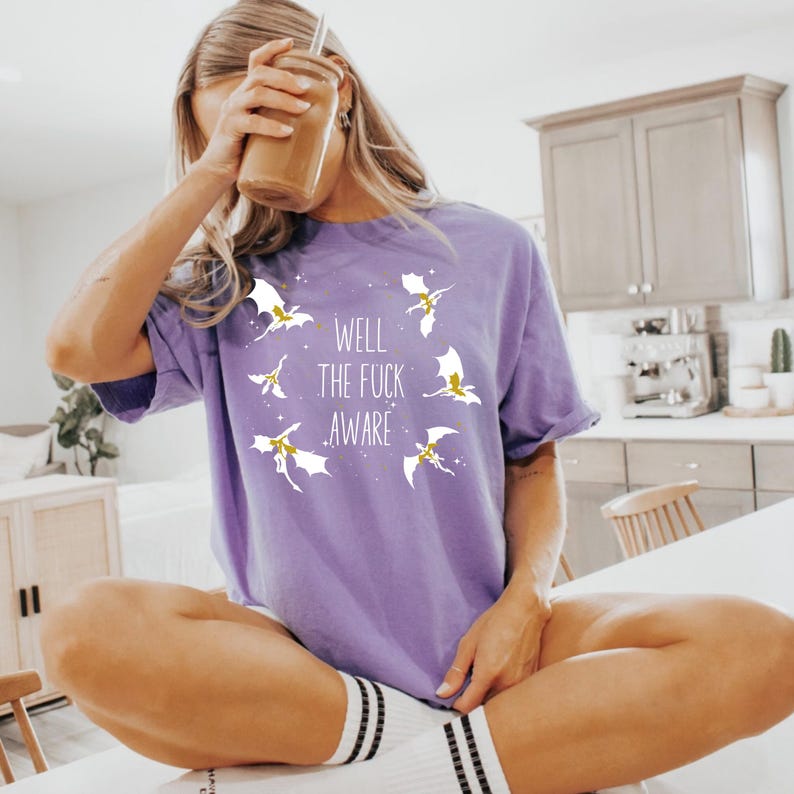 May include: Purple t-shirt with a white graphic of dragons and the text "Well the fuck aware".