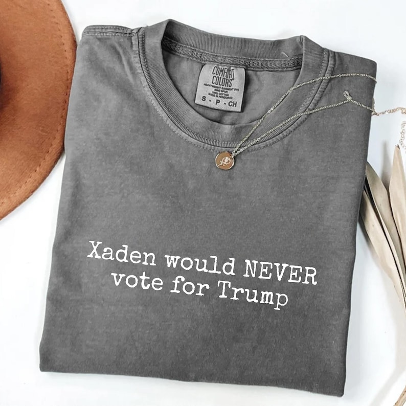 May include: Gray t-shirt with the text "Xaden would NEVER vote for Trump" printed in white.