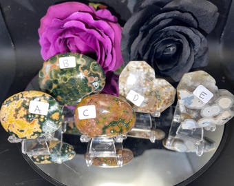 May include: Five polished, oval-shaped, green, brown, and white ocean jasper stones with unique patterns. The stones are on small clear stands labeled A, B, C, D, and E.