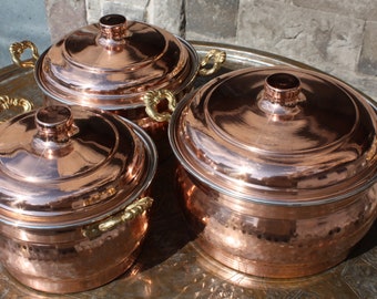 May include: Three copper pots with lids and gold handles. The pots are arranged in a pyramid shape on a decorative tray.