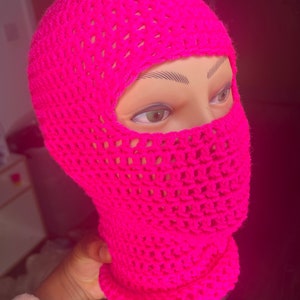 May include: A bright pink crocheted balaclava with a mesh design. The mask covers the head and face, with eye holes for visibility.