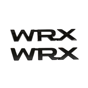May include: Two black, glossy "WRX" emblems. The letters are bold and slightly raised, with a modern font. The emblems are likely for automotive use, designed to be affixed to a vehicle.