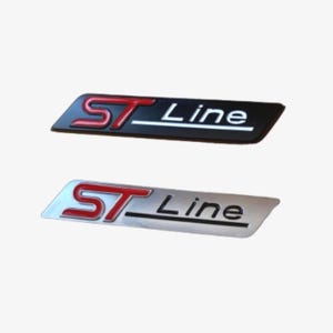 Puede incluir: Dos emblemas de coche ST Line. Uno es negro con texto rojo y blanco, el otro es plateado con texto rojo y blanco. El texto dice "ST Line". Los emblemas son rectangulares con la parte superior e inferior curvadas.