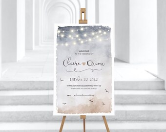 May include: A wedding welcome sign with a watercolor background and string lights. The sign says "Welcome to the wedding of Claire & Orion" and "October 22, 2022".