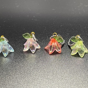 Puede incluir: Cuatro abalorios de flores de vidrio iridiscente con hojas verdes y detalles dorados. Las flores son en tonos de azul, rosa, rojo y amarillo.