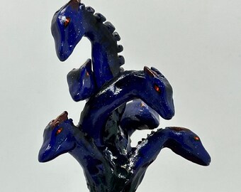 Könnte beinhalten: Eine blaue und schwarze Keramikskulptur einer fünfköpfigen Hydra mit roten Augen. Die Skulptur steht in einem Terrakotta-Pflanztopf mit mehreren Fächern.