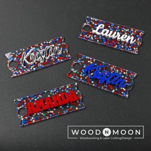 May include: Four personalized acrylic keychains with red, white, and blue glitter. The names "Lauren", "Kristen", "Kristen", and "Amanda" are written on the keychains.