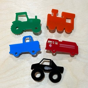 May include: Five toy vehicles made of acrylic plastic. A green tractor, a blue pickup truck, a red fire truck, an orange train, and a black monster truck.