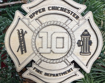 May include: A wooden Christmas ornament shaped like a fire department badge. It features the text "Upper Chichester Fire Department" and the number "10" in the center. The ornament is decorated with a ladder, a fire hydrant, and a rope design.
