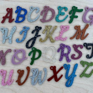 May include: A set of 26 alphabet letter charms, each letter is made of glitter-covered acrylic and is in a different color. The letters are arranged in alphabetical order.