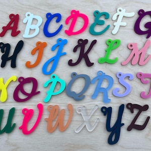 May include: A set of 26 colorful acrylic alphabet letters in a cursive font. Each letter is individually cut and has a hole at the top for hanging.