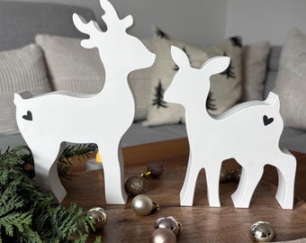 May include: Two white standing deer figurines, one larger than the other, each featuring a small black heart icon on its flank. The deer are crafted with smooth, solid surfaces and are positioned side by side as decorative tabletop ornaments.