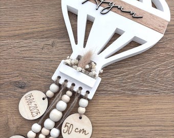 May include: A white and natural wood hot air balloon wall hanging featuring the name Ayan in black script. Four circular wooden tags hang from the base by jute twine and wooden beads, displaying the date 05-06-2025, 50 cm, 3310 g, and 11:39 Uhr.