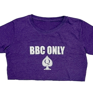 Pu&ograve; includere: Maglietta corta viola con il testo "BBC ONLY" in lettere bianche e un'assegno bianco con una "Q" al suo interno.