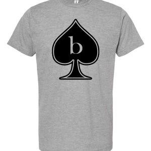 May include: A heather gray t-shirt featuring a black spade symbol with a white letter "b" inside. The spade is outlined in black. The shirt has short sleeves and a crew neck.