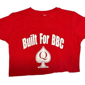 K&ouml;nnte beinhalten: Rotes, bauchfreies T-Shirt mit wei&szlig;em Text "Built For BBC" und einer wei&szlig;en Pikkarte mit einem "Q" darin.