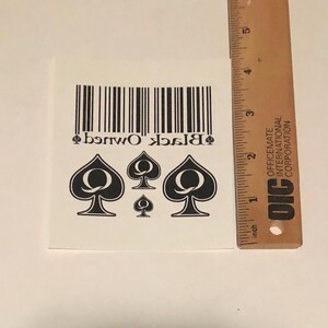 May include: Black Owned temporary tattoo with a barcode and four black queen of spades symbols.