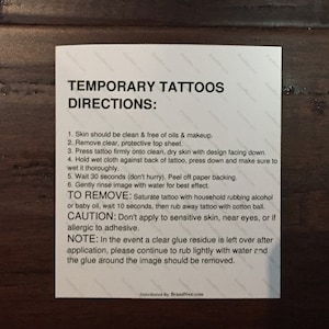 May include: A white rectangular card with instructions for applying temporary tattoos. The card includes directions for application and removal, along with a caution and a note. The text is in black, with the brand name at the bottom.