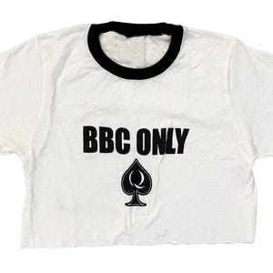 Pu&ograve; includere: Maglietta bianca a maniche corte e bordini neri con la scritta "BBC ONLY" in lettere nere e un asso di picche nero con una "Q" al suo interno.