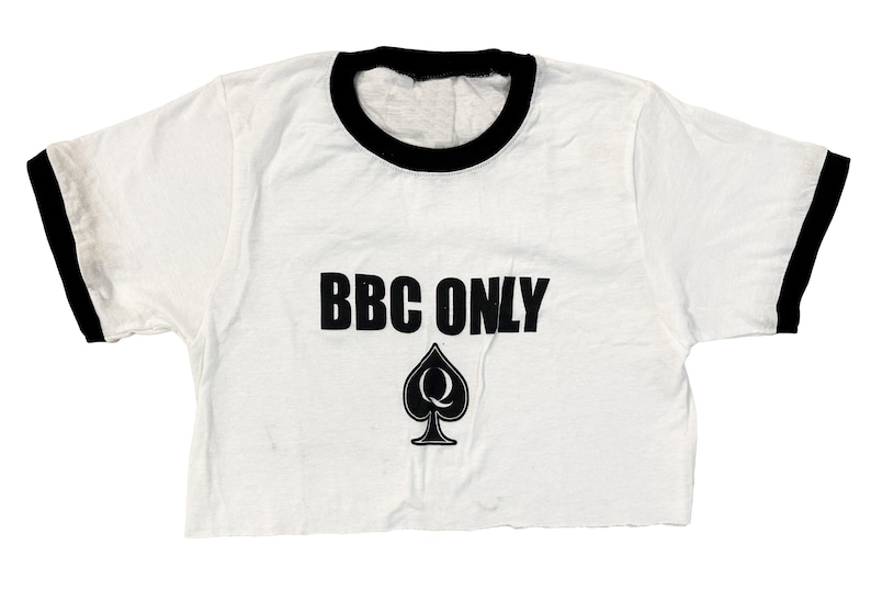 Pu&ograve; includere: Maglietta bianca a maniche corte e bordini neri con la scritta "BBC ONLY" in lettere nere e un asso di picche nero con una "Q" al suo interno.