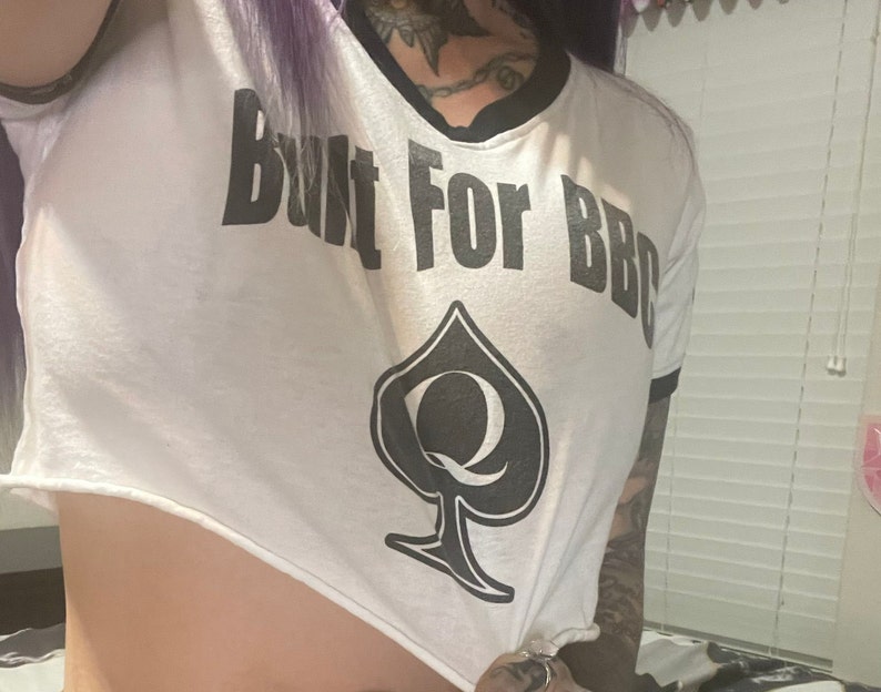 K&ouml;nnte beinhalten: Ein wei&szlig;es Crop-Top mit schwarzem Besatz und dem Text "Built For BBQ" sowie einem schwarzen Pik mit einer K&ouml;nigin darin.
