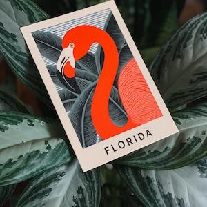May include: A rectangular art print depicting an orange flamingo with a black beak and eye, set against dark green leaves and blue water. The word "FLORIDA" is printed in white at the bottom of the print.