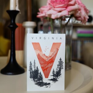 Virginia postcard featuring the letter "V" artistically intertwined with lush forests and majestic mountain peaks. A perfect 4x6" Virginia souvenir celebrating the state’s natural beauty. Printed on premium matte cardstock, ideal for nature lovers, hikers, and adventure seekers.