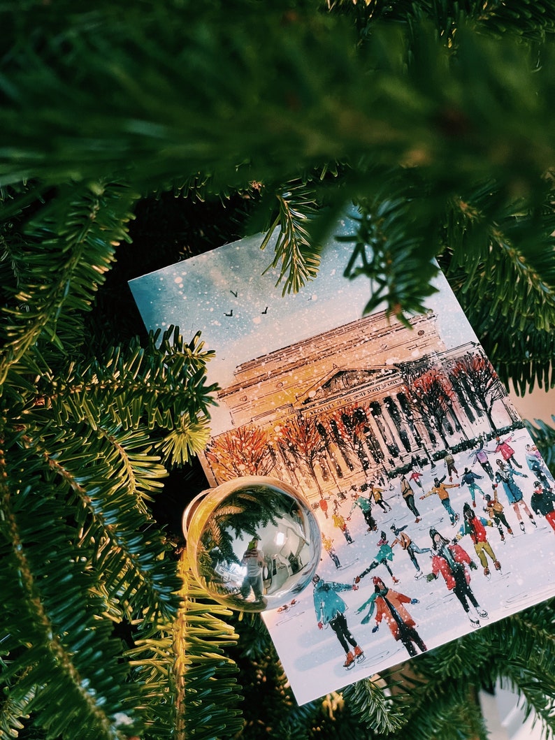 Washington DC Christmas postcard featuring a festive illustration of ice skaters at the National Gallery Sculpture Garden Ice Rink with snowy trees and holiday lights. Perfect DC holiday souvenir, Christmas greeting card, winter travel keepsake, or New Year postcard. Printed on luxe 4x6 matte cardstock, locally made in Washington DC & Virginia. Great for holiday decor lovers, DC travelers, and postcard collectors.