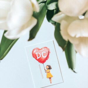 Watercolor illustration of a girl holding a red heart-shaped balloon with "DC" written on it, standing near The Washington Monument. The charming postcard captures the spirit of Washington, DC, with a dreamy, whimsical touch. Perfect for DC lovers, travel enthusiasts, and postcard collectors, this 4x6 design makes a unique souvenir or gift. Printed on premium cardstock with a matte finish, it’s ideal for mailing, framing, or adding to your collection.
