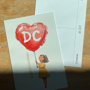Watercolor illustration of a girl holding a red heart-shaped balloon with "DC" written on it, standing near The Washington Monument. The charming postcard captures the spirit of Washington, DC, with a dreamy, whimsical touch. Perfect for DC lovers, travel enthusiasts, and postcard collectors, this 4x6 design makes a unique souvenir or gift. Printed on premium cardstock with a matte finish, it’s ideal for mailing, framing, or adding to your collection.