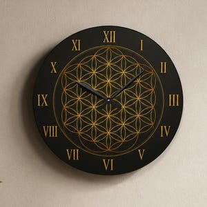May include: A circular wall clock with a matte black face featuring a gold-colored geometric flower of life pattern. The clock has gold-colored Roman numerals from I to XII and two black hands. The design is centered on the clock face.
