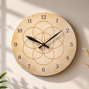 May include: A round wall clock with a beige, textured stone-like face featuring a gold-colored geometric flower of life pattern. The clock has black numerals from 1 to 12 and two black hands centered on the dial, indicating the current time.