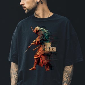 May include: Black t-shirt featuring a digital art design of a samurai warrior with a sword. The warrior is depicted in shades of green, orange, and brown, with the words "CODE BREAKER" printed in white.