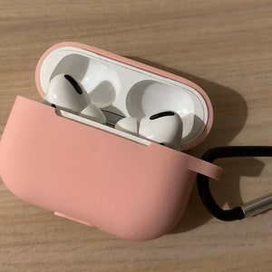 May include: A pink silicone case for wireless earbuds with a black carabiner clip. The case has two white earbuds inside.