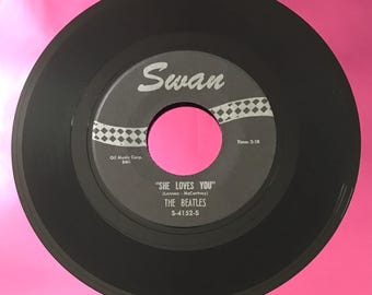 May include: Black vinyl record with a white label. The label has the text "Swan" in a large, cursive font. The record is titled "She Loves You" by "The Beatles". The record number is "S-4152-5".