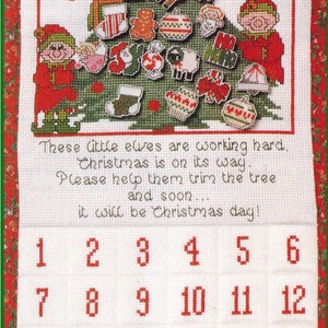 May include: A white felt advent calendar with a green Christmas tree and elves. The calendar has 24 numbered pockets, each with a different Christmas ornament. The text reads: "These little elves are working hard. Christmas is on its way. Please help them trim the tree and soon... it will be Christmas day!"