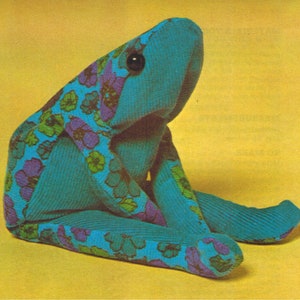 Peut inclure: Un jouet en peluche de grenouille bleue avec un motif floral. La grenouille est assise les jambes croisées et a un œil noir.