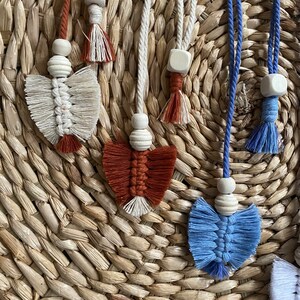 May include: Four handmade macrame wall hangings with wooden beads and tassels. The hangings are in shades of white, blue, red, and brown.