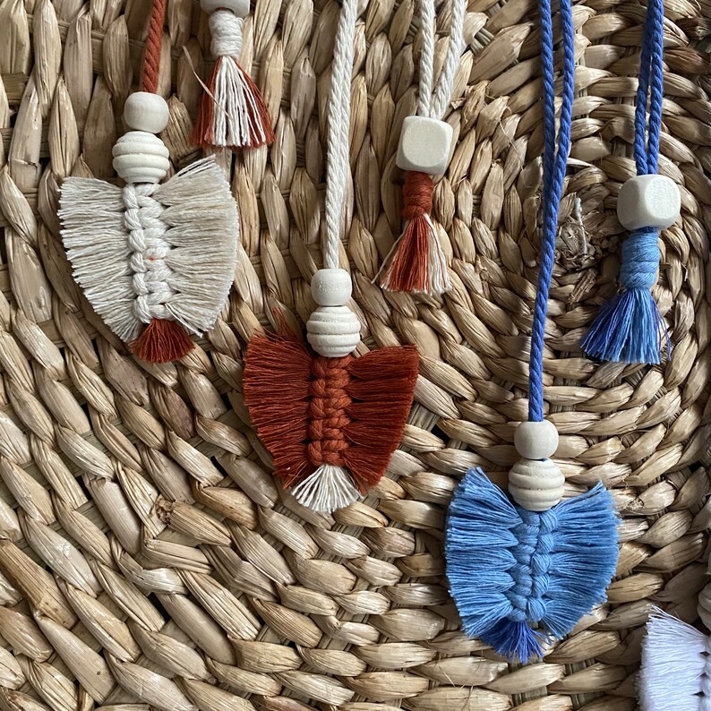 May include: Four handmade macrame wall hangings with wooden beads and tassels. The hangings are in shades of white, blue, red, and brown.