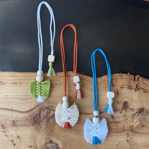 May include: Three handmade macrame tassel keychains with wooden beads and different colored tassels. The tassels are green, white, and blue.