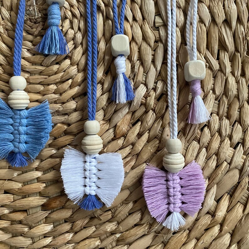 May include: Three macrame tassel keychains with wooden beads and different colored tassels. The tassels are blue, white, and purple.