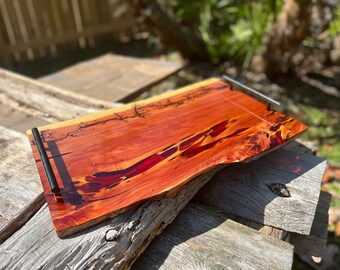 Puede incluir: Una bandeja de servir de madera grande con veta de madera natural y detalles de resina roja. La bandeja tiene dos asas de metal negro a los lados.