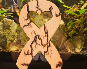 Puede incluir: Una cinta de madera con un corte en forma de corazón en el centro. La cinta está decorada con un diseño de pirograbado que se asemeja a venas o ramas. La cinta es de color marrón claro y tiene un acabado de madera natural.