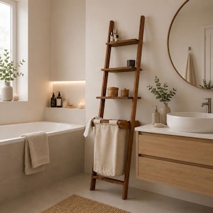 Può includere: Una scaffalatura a scala in legno marrone scuro con tre ripiani aperti e una sezione inferiore integrata con un cesto portabiancheria in tessuto beige sospeso. I ripiani contengono piccole bottiglie, contenitori e oggetti decorativi.