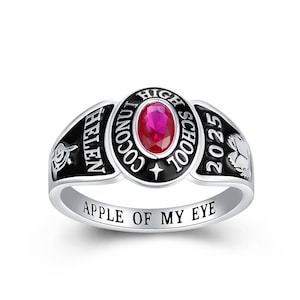 May include: A silver class ring with a black enamel band and a red gemstone. The ring says "Coconut Helen High School 2025" and "Apple of My Eye" on the band.